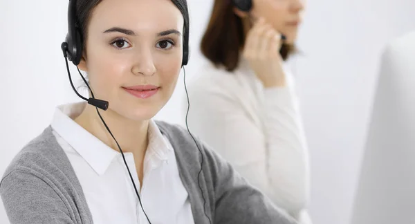 Centro de llamadas. Mujer vestida casual trabajando en auriculares con diversos colegas en la oficina. Concepto empresarial —  Fotos de Stock