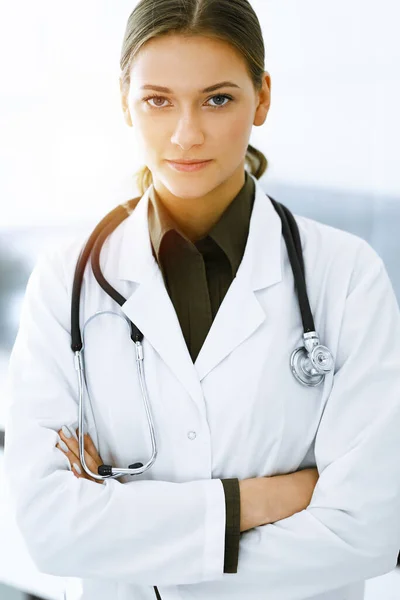 Žena-doktorka stojí a dívá se na kameru na slunné klinice. Perfektní lékařská služba. Léky a zdravotní péče — Stock fotografie