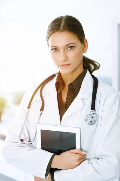 Mujer-médico de pie y mirando a la cámara en la clínica soleada. Un servicio médico perfecto. Medicina y asistencia sanitaria — Foto de Stock