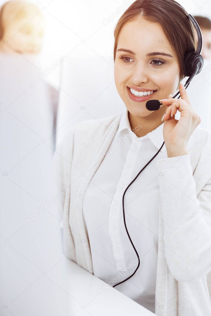 Call center in sunny office. Group of diverse operators at work. Beautiful woman in headset communicating with customers of telemarketing service. Business concept
