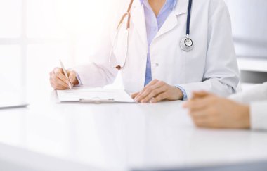 Güneşli klinikteki tıbbi muayenede oturan ve konuşan kimliği belirsiz kadın-doktor ve kadın hasta, yakın plan. Tıp konsepti