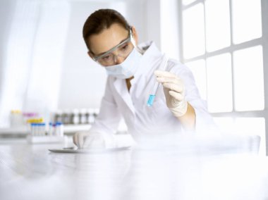 Kadın laboratuvar asistanı mavi sıvıyla test tüpünü analiz ediyor. Tıp, sağlık ve araştırma konsepti