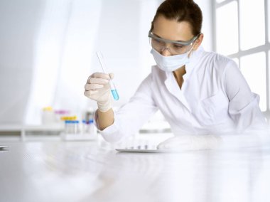 Kadın laboratuvar asistanı mavi sıvıyla test tüpünü analiz ediyor. Tıp, sağlık ve araştırma konsepti