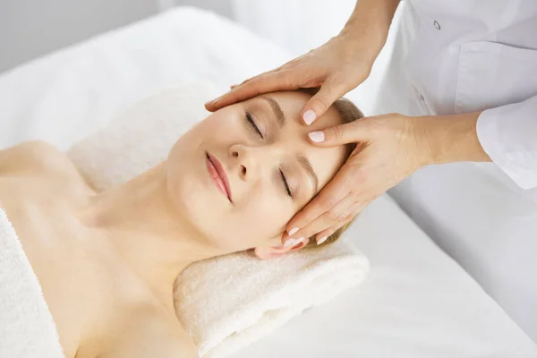 Beautiful caucasian woman enjoying facial massage with closed eyes in spa salon. Relaxing treatment in medicine and Beauty concept — Stock Photo, Image