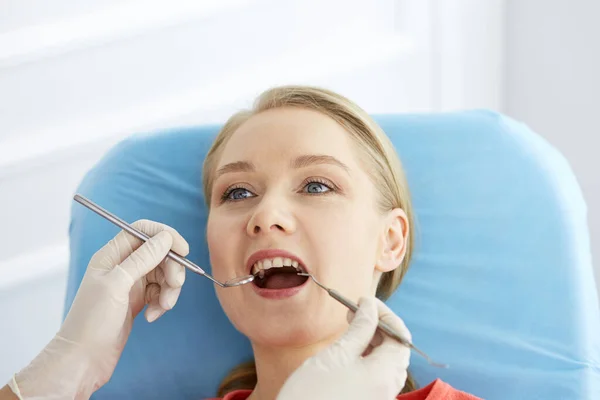 Uśmiechnięta biała kobieta jest badana przez dentystę w klinice stomatologicznej. Zdrowe zęby i medycyna, koncepcja stomatologii — Zdjęcie stockowe