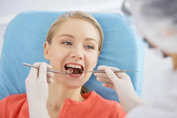 Uśmiechnięta biała kobieta jest badana przez dentystę w klinice stomatologicznej. Zdrowe zęby i medycyna, koncepcja stomatologii — Zdjęcie stockowe