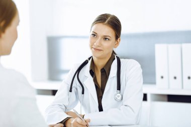 Kadın doktor ve hasta hastane ofisinde oturuyor ve konuşuyor. Yeşil renkli bluz terapiste uygun.