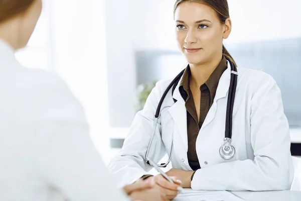 Mujer-médico y paciente sentados y hablando en el consultorio del hospital. Blusa de color verde se adapta al terapeuta — Foto de Stock