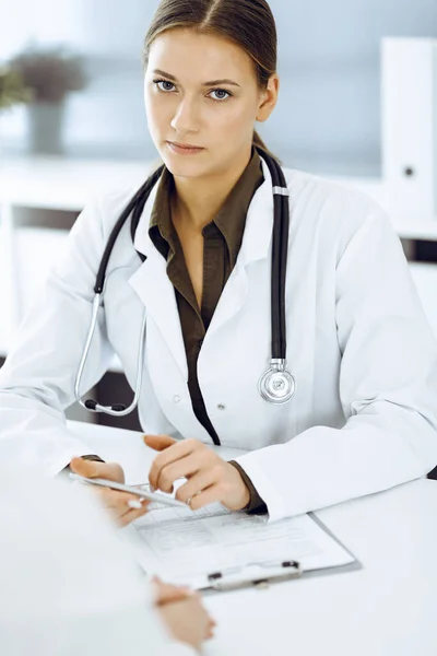 Mujer-médico y paciente sentados y hablando en el consultorio del hospital. Blusa de color verde se adapta al terapeuta — Foto de Stock