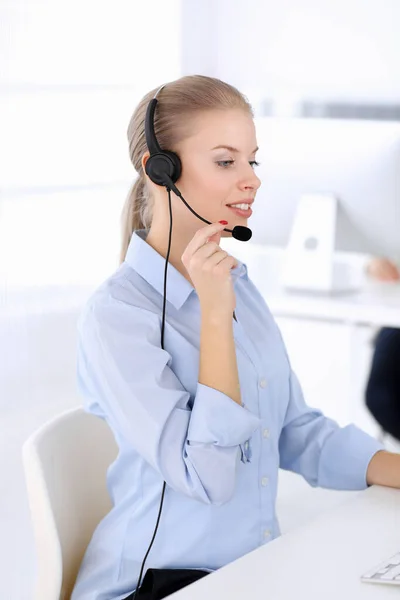 Llama a la oficina central. Hermosa mujer rubia usando computadora y auriculares para consultar a los clientes en línea. Grupo de operadores que trabajan como ocupación de servicio al cliente. Concepto gente de negocios — Foto de Stock