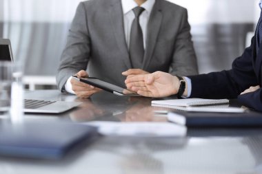 Bilinmeyen işadamı, modern ofisteki cam masada otururken tablet bilgisayar kullanıyor ve iş arkadaşıyla birlikte çalışıyor. Takım çalışması ve ortaklık kavramı