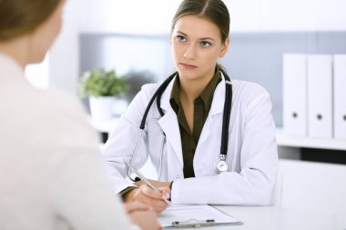 Kadın doktor ve hasta hastane muayenehanesinde oturup konuşuyorlar. Yeşil renkli bluz terapiste yakışır. Tıp ve sağlık hizmetleri kavramı