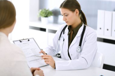 Kadın doktor ve hasta hastane muayenehanesinde oturup konuşuyorlar. Yeşil renkli bluz terapiste yakışır. Tıp ve sağlık hizmetleri kavramı