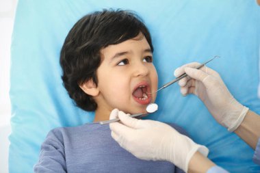 Doktor muayenesi sırasında ağzı açık bir şekilde diş sandalyesinde oturan küçük Arap çocuk. Dişçi muayenehanesi. Tıp ve stomatoloji kavramı