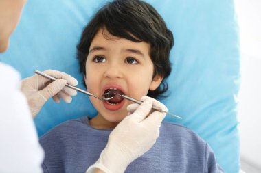 Doktor muayenesi sırasında ağzı açık bir şekilde diş sandalyesinde oturan küçük Arap çocuk. Dişçi muayenehanesi. Tıp ve stomatoloji kavramı