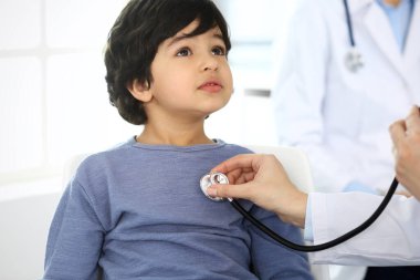 Doktor steteskopla çocuk bir hastayı muayene ediyor. Doktor randevusunda tatlı bir Arap çocuk. Tıp ve sağlık hizmetleri kavramı