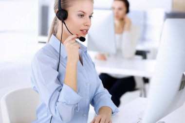 Merkezi ara. İnternette müşterilere danışmak için bilgisayar ve kulaklık kullanan güzel sarışın kadın. Müşteri hizmetleri işgali olarak çalışan bir grup operatör. İş adamları konsepti