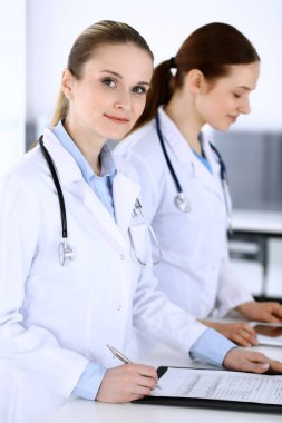 Hastanede çalışan bir grup doktor. Doktor resepsiyonda beklerken tıbbi belge ya da reçete dolduruyor. Tıp ve sağlık hizmetleri kavramındaki veriler