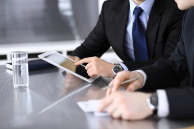 İşadamı tablet bilgisayar kullanıyor ve iş arkadaşı ya da ortağıyla modern ofiste cam masada çalışıyor. Yakın plan. Toplantıda bilinmeyen iş adamları var. Takım çalışması ve ortaklık kavramı