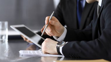 İşadamı tablet bilgisayar kullanıyor ve iş arkadaşı ya da ortağıyla modern ofiste cam masada çalışıyor. Yakın plan. Toplantıda bilinmeyen iş adamları var. Takım çalışması ve ortaklık kavramı