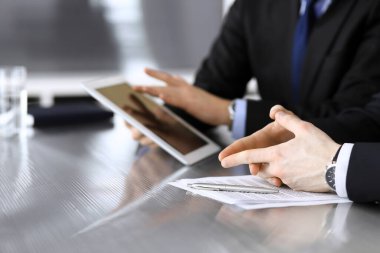 İşadamı tablet bilgisayar kullanıyor ve iş arkadaşı ya da ortağıyla modern ofiste cam masada çalışıyor. Yakın plan. Toplantıda bilinmeyen iş adamları var. Takım çalışması ve ortaklık kavramı