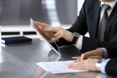 İşadamı tablet bilgisayar kullanıyor ve iş arkadaşı ya da ortağıyla modern ofiste cam masada çalışıyor. Yakın plan. Toplantıda bilinmeyen iş adamları var. Takım çalışması ve ortaklık kavramı