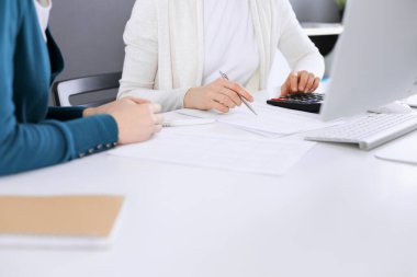 Mali durumu kontrol eden ya da vergi formları için hesap makinesinin geliri ile sayan, elleri yakın çekim. İş kadını, iş yerinde iş arkadaşıyla birlikte mavi tonda oturuyor. Vergi ve