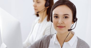 Merkezi ara. Ofisteki çeşitli iş arkadaşlarıyla kulaklık takan sıradan giyinmiş bir kadın. İş konsepti