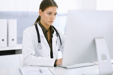 Hastane ofisindeki masada otururken bilgisayar başında daktilo yazan kadın doktor. Hekim iş başında. Tıp ve sağlık alanlarındaki veriler