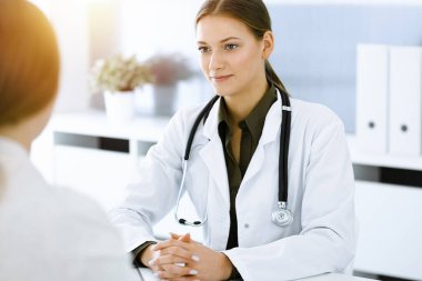 Kadın-doktor ve hasta güneşli hastane ofisinde oturup konuşuyorlar. Yeşil renkli bluz terapiste yakışır. Tıp konsepti