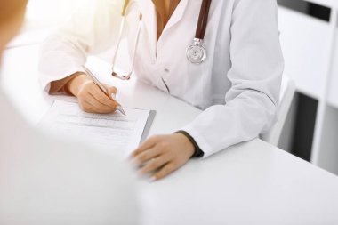 Güneşli klinikteki tıbbi muayenede oturan ve konuşan kimliği belirsiz kadın-doktor ve kadın hasta, yakın plan. İlaç geçmişini dolduran bir terapist. Tıp konsepti