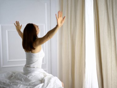 Bir kadın uyandıktan sonra yatakta geriniyor, geriye bakıyor, bir güne mutlu ve rahat giriyor iyi bir gece uykusundan sonra. Esmer için günaydın ve yeni bir gün. Hafta sonu kavramı, tatiller