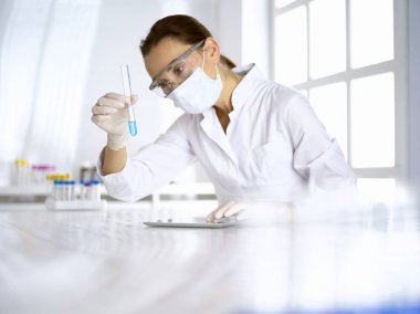 Kadın laboratuvar asistanı mavi sıvıyla test tüpünü analiz ediyor. Tıp, sağlık ve araştırma konsepti