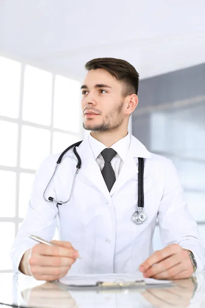 Dokter man vullen medicatie geschiedenis administratie formulier tijdens het zitten aan het glazen bureau in het medisch kantoor of kliniek. Concept geneeskunde en gezondheidszorg — Stockfoto