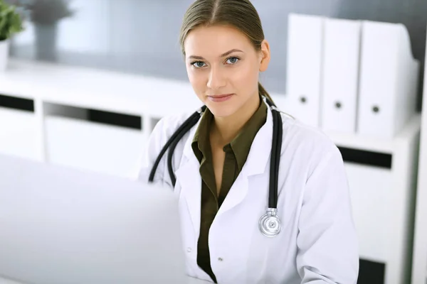 Doctor typing on pc computer while sitting at the desk in hospital office. Physician woman at work. Data in medicine and healthcare