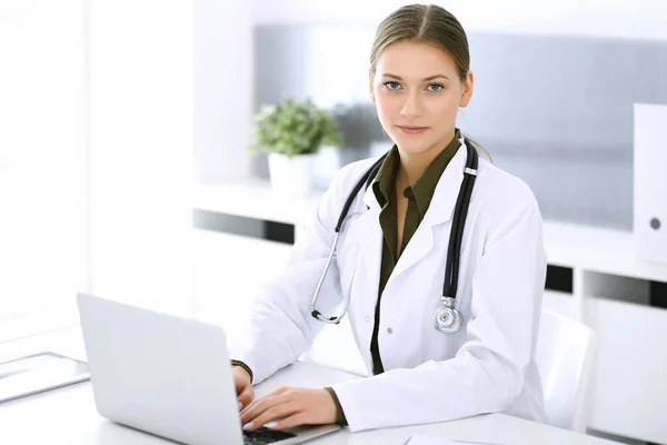 Médico escribiendo en el ordenador portátil mientras está sentado en el escritorio en la oficina del hospital. Mujer médica en el trabajo. Datos en medicina y asistencia sanitaria — Foto de Stock