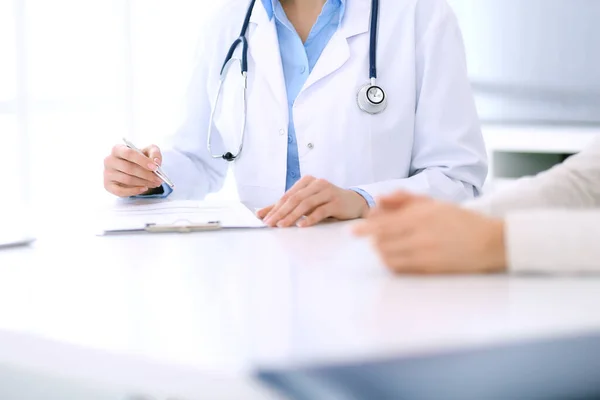 Doctora y paciente sentadas y hablando en el examen médico en el consultorio del hospital, de cerca. Médico llenando registros de historial de medicamentos. Concepto de medicina y salud — Foto de Stock