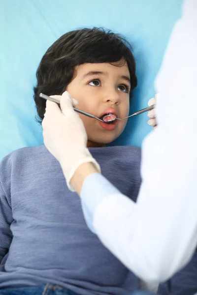 Pequeño chico árabe sentado en la silla dental con la boca abierta durante la revisión oral mientras que el médico. Visita al consultorio del dentista. Concepto de medicina y estomatología —  Fotos de Stock
