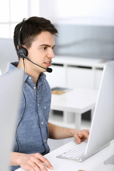 Group of operators at work. Call center. Focus on young man receptionist in headset at customer service. Business concept and casual clothing style — Stock Photo, Image