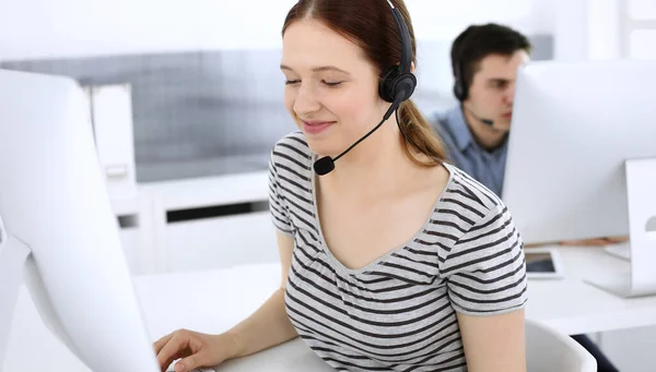 Group of operators at work. Call center. Focus on beautiful woman receptionist in headset at customer service. Business concept and casual striped clothing style — Stock Photo, Image