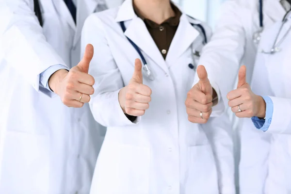Bir grup modern doktor hastane ofisinde baş parmakları havada bir takım gibi duruyorlar. Doktorlar hastaları muayene etmeye ve yardım etmeye hazır. Tıbbi yardım, sağlık sigortası, en iyi hastalık tedavisi ve ilaç