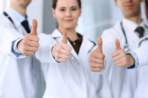 Bir grup modern doktor hastane ofisinde baş parmakları havada bir takım gibi duruyorlar. Doktorlar hastaları muayene etmeye ve yardım etmeye hazır. Tıbbi yardım, sağlık sigortası, en iyi hastalık tedavisi ve ilaç