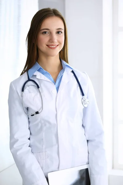 Doctora mujer feliz y alegre, mientras que de pie en la oficina del hospital en el fondo de luz. Concepto de medicina y salud — Foto de Stock