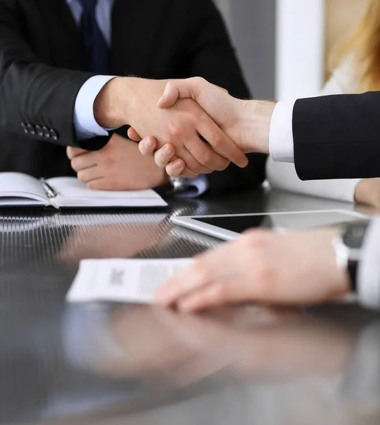 Empresario estrechando la mano con su colega o compañero por encima del escritorio de cristal en la oficina moderna, de cerca. Gente de negocios desconocida en la reunión. Trabajo en equipo, asociación y concepto de apretón de manos — Foto de Stock