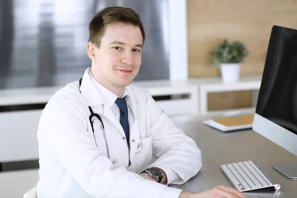 Доктор людина сидить за комп'ютером на робочому місці в клініці або лікарняному кабінеті. Медичний головний убір та концепція медицини — стокове фото
