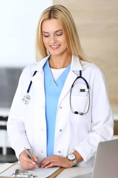 病院で働く医師の女性は彼女の職業に興奮し、幸せ。ブロンドの医師は薬の履歴と検査結果を制御します。医学と医療の概念 — ストック写真