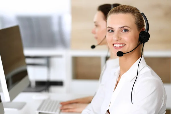 Call center. Donna d'affari felice ed eccitata che utilizza cuffie mentre consulta i clienti online. Ufficio assistenza clienti o reparto telemarketing. Gruppo sorridente di operatori al lavoro — Foto Stock