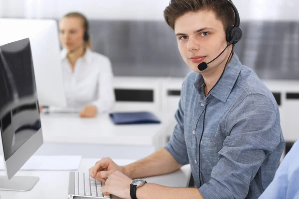 Centro de llamadas. Grupo de operadores vestidos casuales en el trabajo. Enfócate en el joven empresario con auriculares en la oficina de servicio al cliente. Telesales en el negocio —  Fotos de Stock