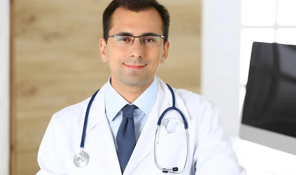 Doctor man sitting at the desk at his working place and smiling at camera. Perfect medical service in clinic. Happy future of medicine and healthcare — Stock Photo, Image