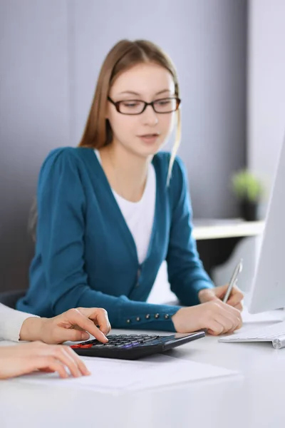 Contabilista verificando ficha financeira ou contando por calculadora de renda para a forma de imposto, mãos close-up. Mulher de negócios sentada e trabalhando com colega na mesa no escritório tonificada em azul. Impostos e — Fotografia de Stock